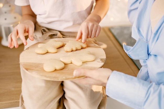 Foto recortada de biscoitos de gengibre em uma bandeja de madeira segurando por mãe e filha