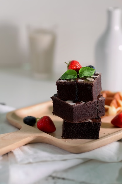 Foto recortada de brownies de pilha de chocolate com morangos e mirtilos, decorados na bandeja de madeira