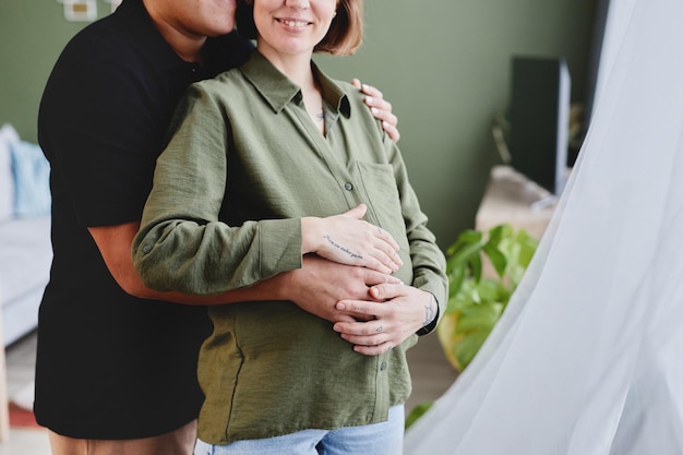 Foto recortada de casal gay feliz esperando bebê e abraçando amorosamente no espaço de cópia interior em casa