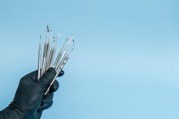 Foto recortada de dentista profissional em luvas médicas pretas com ferramentas dentárias Conceito dental isolado em fundo azul