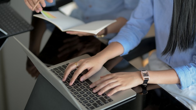 Foto recortada de digitação feminina no laptop enquanto seu colega de trabalho informava sobre o projeto