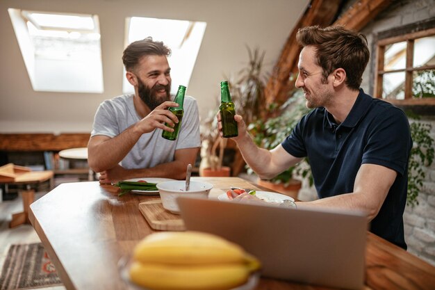 Foto recortada de dois amigos do sexo masculino comendo na cozinha