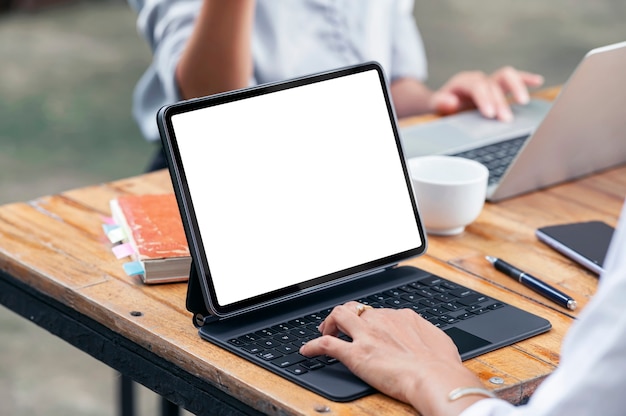 Foto recortada de dois jovens trabalhando juntos, usando laptop e tablet enquanto está sentado à mesa ao ar livre.