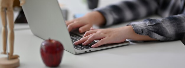 Foto recortada de empresária digitando no laptop na mesa de escritório branco