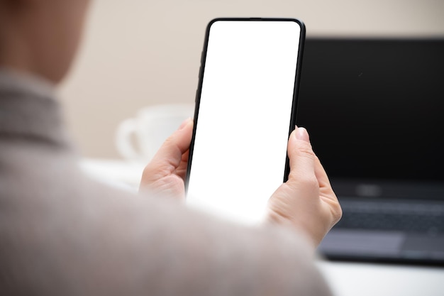 Foto recortada de empresária olhando para smartphone de tela em branco na mão de uma mulher de escritório moderno segurando o telefone com tela branca no escritório mulher usando telefone celular no local de trabalho