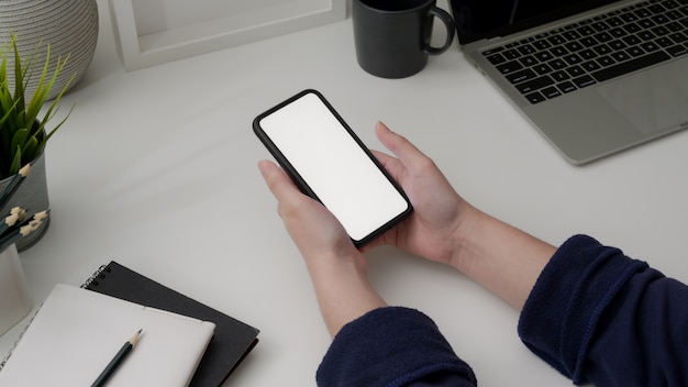 Foto recortada de empresária segurando o smartphone de tela em branco na mesa branca