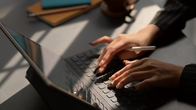 Foto recortada de empresárias digitando no tablet de tela em branco no escritório escuro moderno