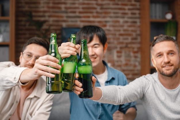 Foto recortada de garrafas de cerveja nas mãos de homens assistindo a um jogo de futebol