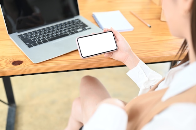 Foto recortada de jovem freelancer masculino segurando tela em branco smartphone em seu confortável espaço de trabalho.