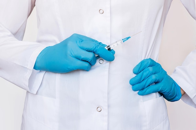 Foto recortada de jovem médica em um jaleco branco segurando seringa com as mãos em luvas azuis