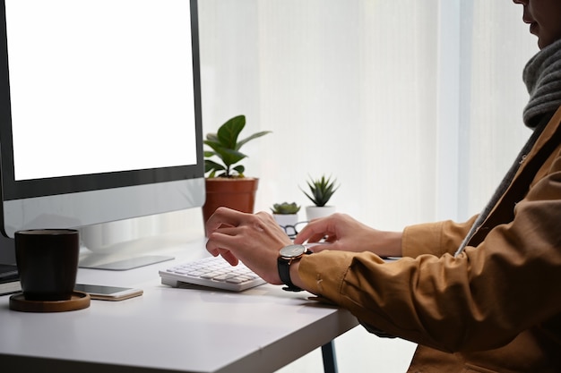 Foto recortada de jovem olhando para a tela do computador e trabalhando no projeto em um escritório moderno.