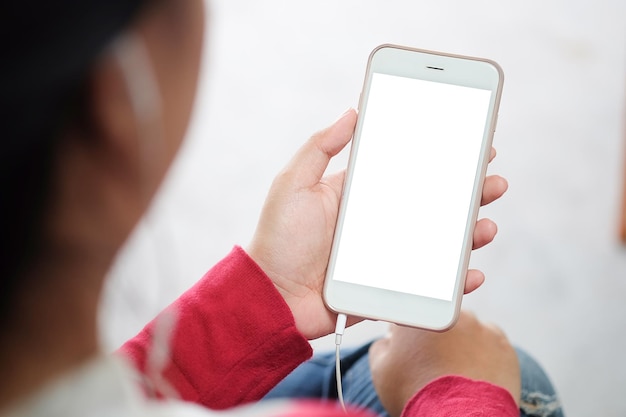 Foto recortada de jovem relaxando no sofá confortável enquanto segura o smartphone com tela em branco nas mãos