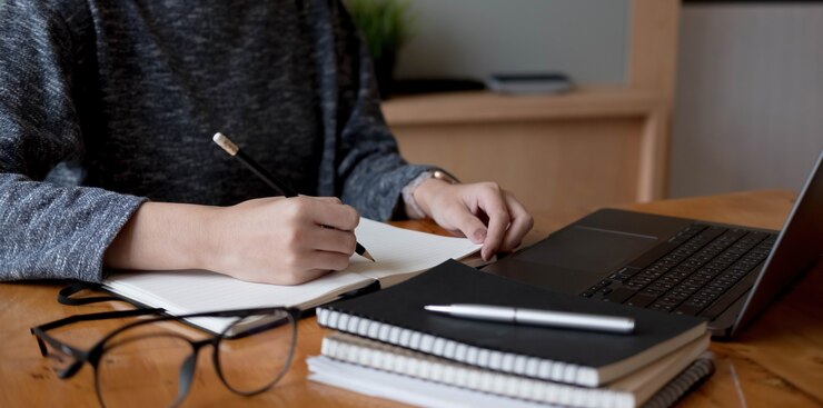 Foto recortada de mão de mulher escrevendo fazendo lista fazendo anotações no bloco de notas trabalhando ou aprendendo on-line com o laptop em casa