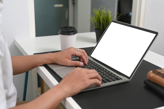 Foto recortada de mãos de homem digitando no computador laptop em sua mesa de escritório.