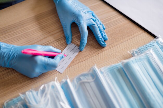 Foto recortada de mãos ocupadas luvas de látex tendência de negócios organização embalagem máscara facial contra gripe máscaras médicas difusão global escrever pedido verificar endereço preparar conjuntos entrega escritório em casa dentro de casa