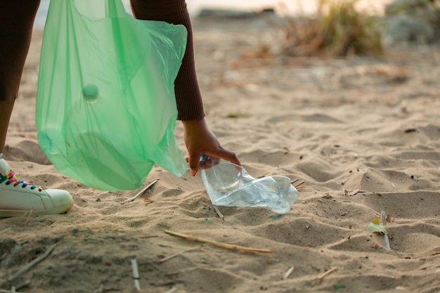 Foto recortada de mulher africana coletando lixo derramado de areia na praia em saco plástico verde Poluição ecológica