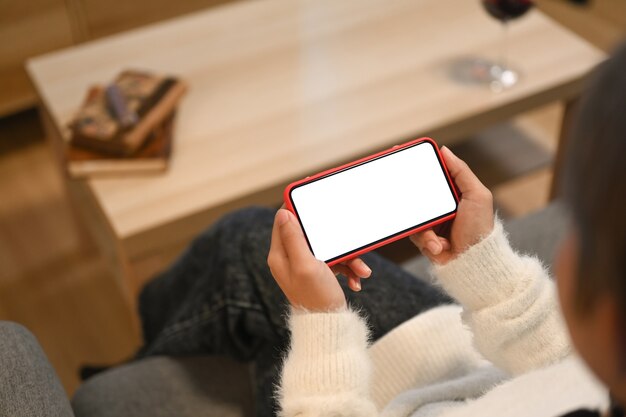 Foto recortada de mulher assistindo mídia em um telefone inteligente e sentada em um sofá em casa.