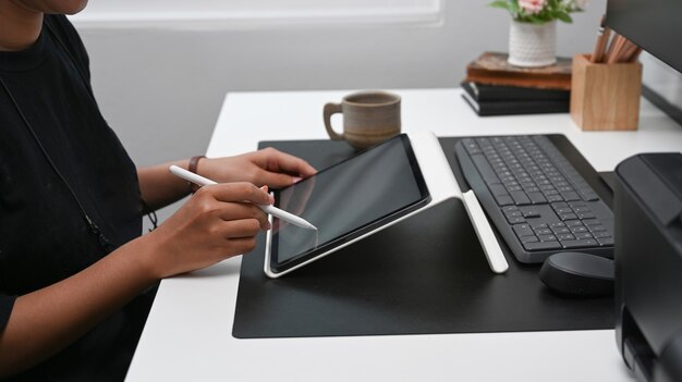 Foto recortada de mulher criativa segurando a caneta stylus e trabalhando com tablet digital na mesa do escritório.