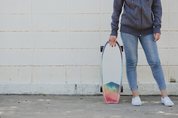 Foto recortada de mulher em roupa casual com surfskate contra a parede de concreto. conceito de estilo de vida ativo