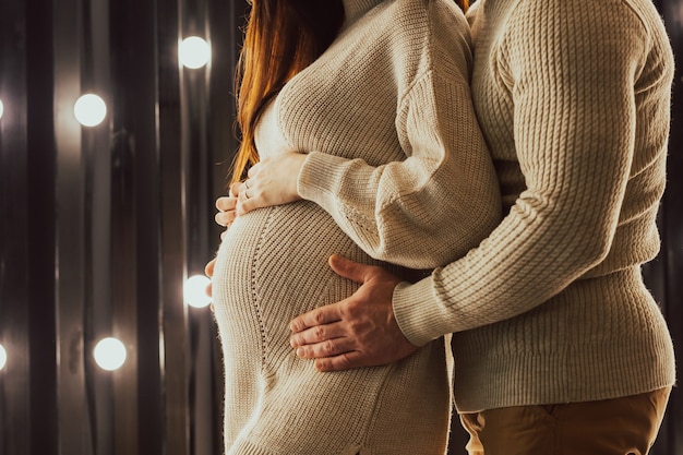 Foto recortada de mulher grávida e seu marido de blusas abraçando a barriga