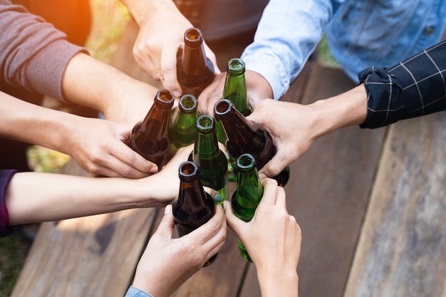 Foto recortada de pessoas segurando copos de cerveja, celebrando a festa de acampamento de verão ao ar livre. Amigos tilintando uma garrafa de cerveja durante o acampamento ao ar livre