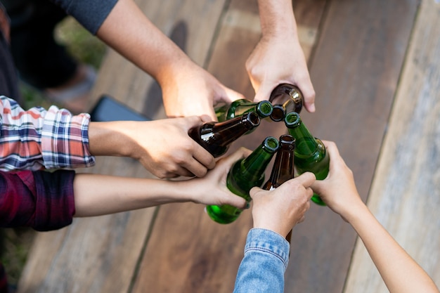 Foto recortada de pessoas segurando copos de cerveja, celebrando a festa de acampamento de verão ao ar livre. Amigos tilintando uma garrafa de cerveja durante o acampamento ao ar livre