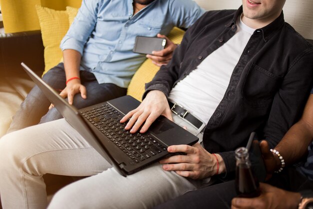 Foto recortada de três colegas homens trabalhando no laptop. Alunos de amigos sentados juntos no sofá, assistindo a um vídeo, navegando na Internet juntos.