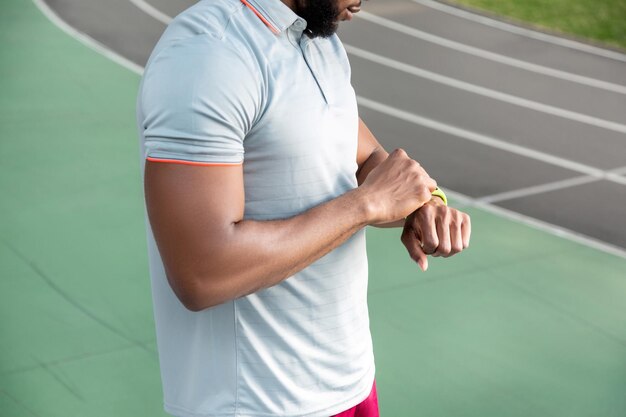 Foto recortada de um atleta afro-americano em pé no estádio enquanto olhava para seu rastreador fitbit