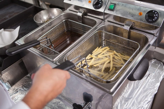 Foto recortada de um chef profissional preparando batatas fritas em uma frigideira de óleo quente