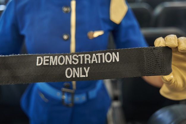 Foto recortada de um cinto de segurança para demonstração de instruções de segurança nas mãos de uma aeromoça profissional