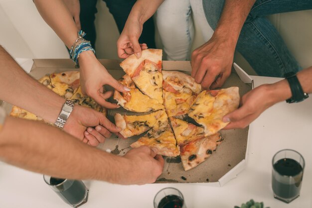 Foto recortada de um grupo de amigos tomando fatias de pizza juntos.