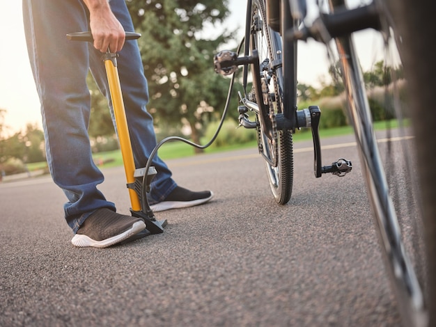 Foto recortada de um jovem usando uma bomba enquanto inflando o pneu de sua bicicleta em pé