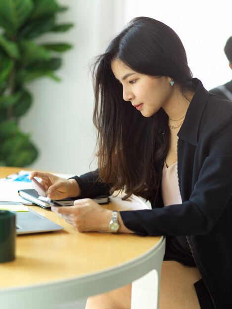 Foto recortada de uma empresária pagando online com smartphone e cartão de crédito na sala do escritório