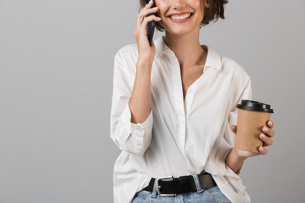 Foto recortada de uma jovem mulher de negócios feliz falando ao celular e bebendo café