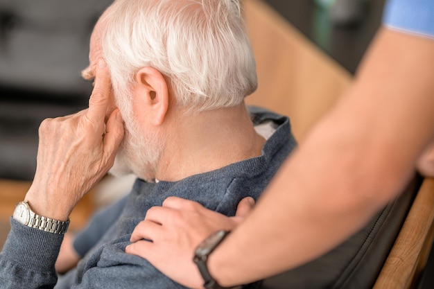 Foto foto recortada de uma mão de cuidador acariciando um homem caucasiano sênior de cabelos grisalhos no ombro