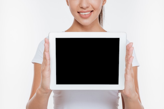 Foto recortada de uma mulher alegre segurando um tablet digital e mostrando a tela na frente, isolada na parede branca