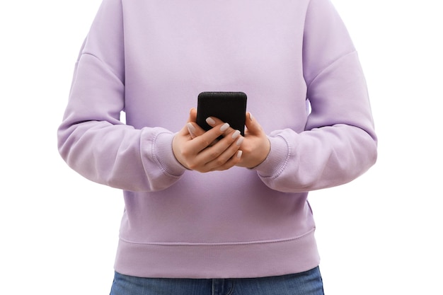 Foto recortada de uma mulher em um suéter de lavanda e jeans está segurando o smartphone com as duas mãos