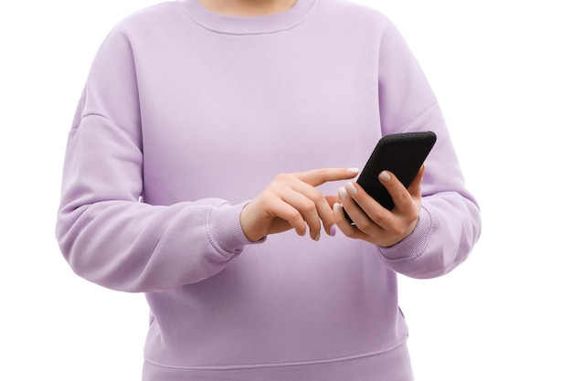 Foto recortada de uma mulher em um suéter de lavanda e jeans está segurando o smartphone na mão apontando tocando na tela