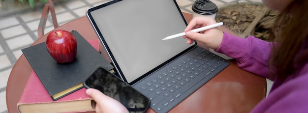 Foto recortada de universitária tomando nota curta no tablet enquanto procurava informações no smartphone