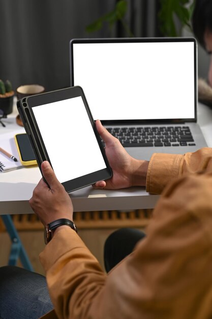 Foto recortada do empresário sentado na frente do computador portátil e segurando o tablet digital.