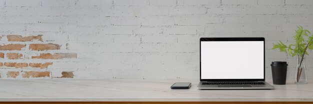 Foto recortada do espaço de trabalho contemporâneo com laptop de tela em branco, smartphone, decoração e espaço de cópia na mesa de mármore