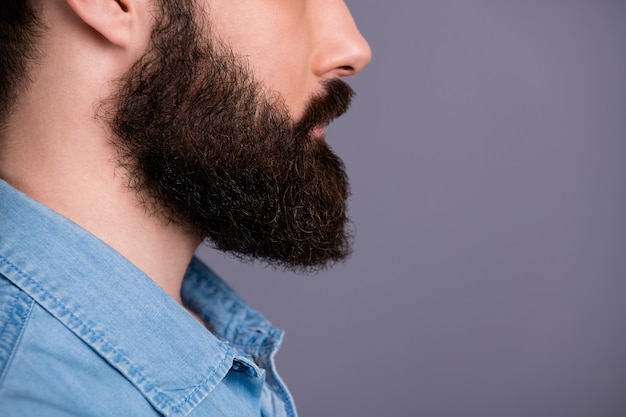 Foto recortada do perfil do cara focado na cópia do espaço mostra sua barba bem cuidada após o procedimento de cuidados corporais do salão de spa. Use jeans elegantes isolados sobre a parede de cor cinza