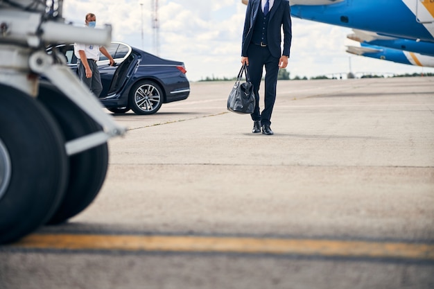 Foto recortada de un empresario que lleva una bolsa de lona caminando por los aviones