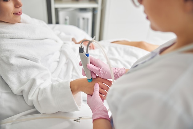 Foto recortada de una esteticista con guantes de látex tratando la piel de las manos de su paciente