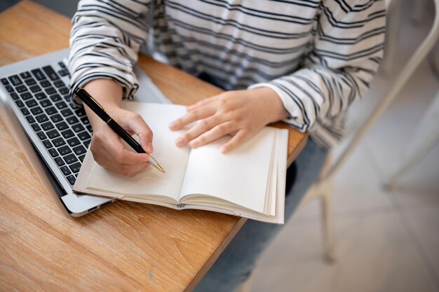 Una foto recortada de una estudiante haciendo la tarea o tomando notas en su cuaderno en una mesa