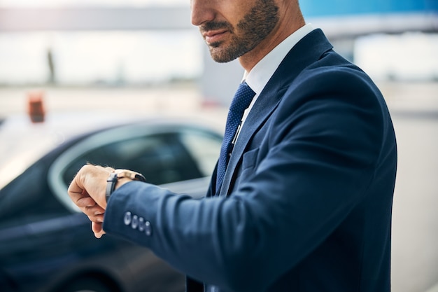 Foto recortada de un hombre bien vestido que levanta la mano para comprobar la hora en su reloj de pulsera