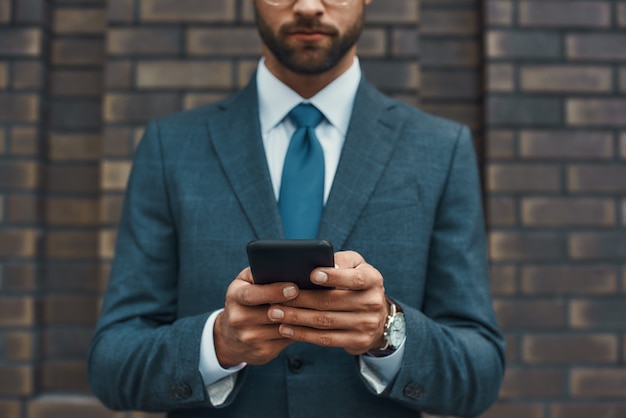 Foto recortada de un hombre de negocios en ropa formal y usando su teléfono inteligente mientras está de pie