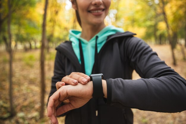 Foto recortada de increíble joven mujer bonita fitness al aire libre en el parque mirando el reloj.