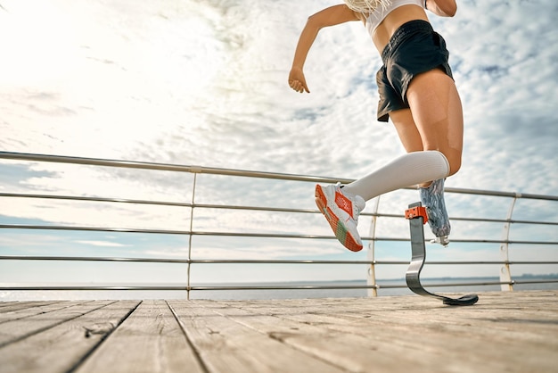 Foto recortada jovem com perna protética correndo na ponte Treinamento esportivo feminino ao ar livre