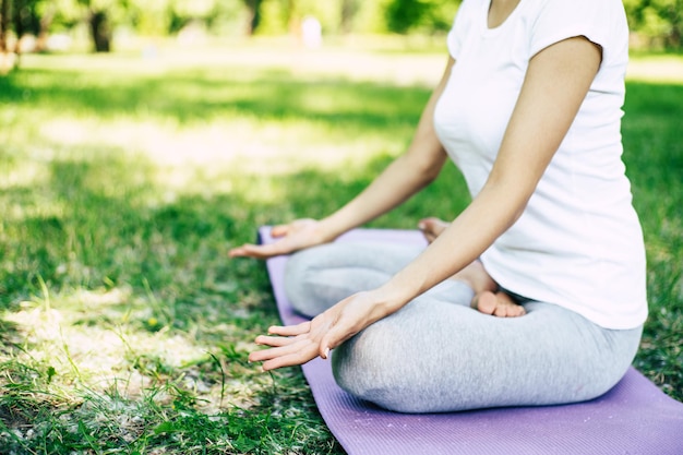 Foto recortada de joven delgada en ropa de ejercicio mientras está sentada en posición de loto en la estera de yoga. Yoga matutino. Estilo de vida saludable